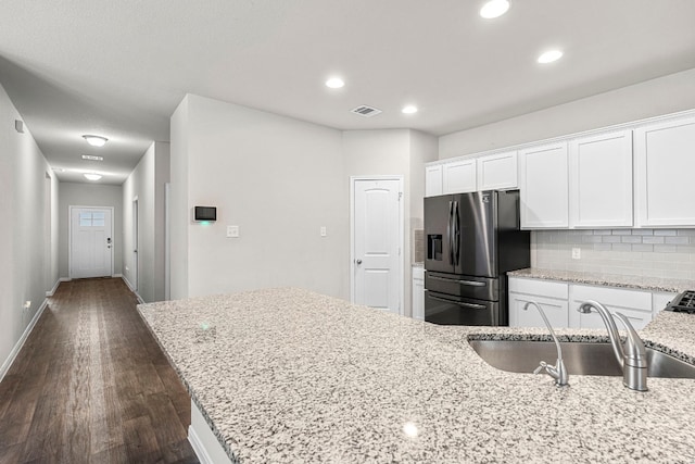 kitchen featuring stainless steel refrigerator with ice dispenser, decorative backsplash, white cabinets, a sink, and light stone countertops