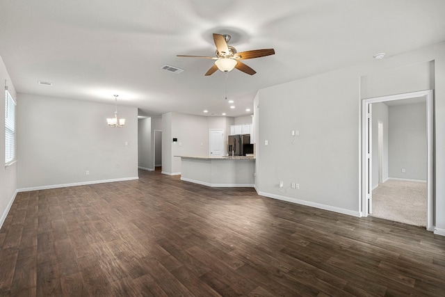 unfurnished living room with ceiling fan with notable chandelier, dark wood-style flooring, visible vents, and baseboards