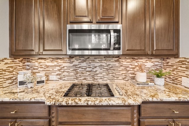 kitchen with backsplash, dark brown cabinets, light stone counters, and stainless steel appliances