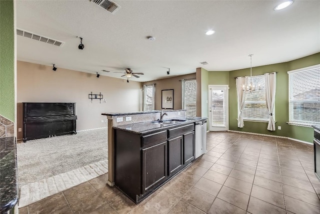 kitchen with pendant lighting, sink, dishwasher, a kitchen island with sink, and dark stone countertops