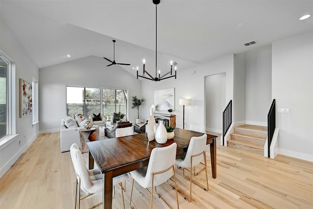 dining room with ceiling fan with notable chandelier, light hardwood / wood-style floors, and vaulted ceiling