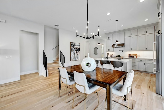 dining area with light wood-type flooring, sink, and an inviting chandelier