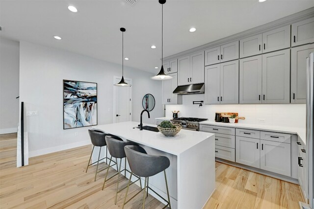 kitchen with high end range, tasteful backsplash, a kitchen island with sink, and hanging light fixtures