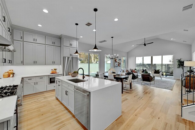 kitchen with appliances with stainless steel finishes, ceiling fan with notable chandelier, sink, pendant lighting, and a center island with sink