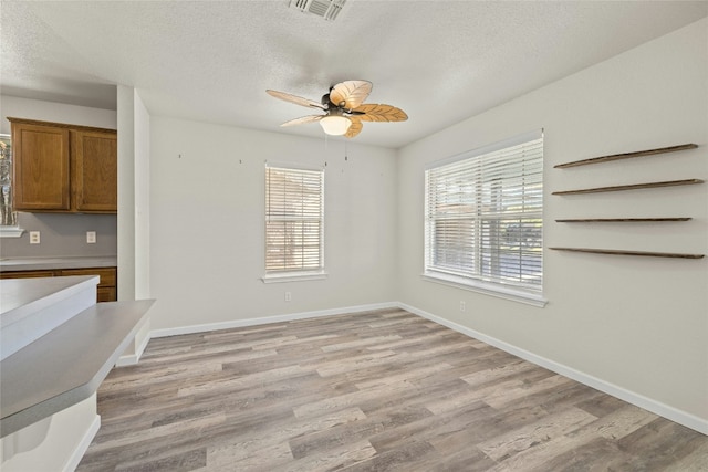 unfurnished dining area with ceiling fan, a healthy amount of sunlight, a textured ceiling, and light wood-type flooring