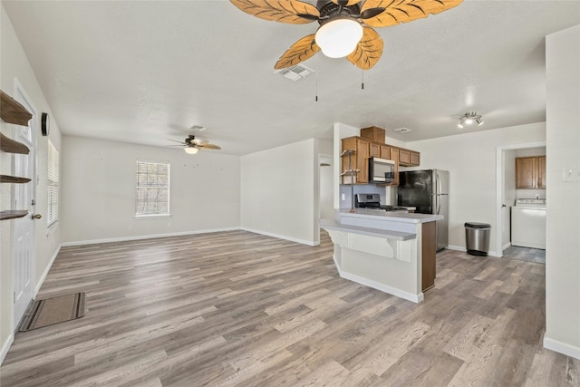 kitchen with kitchen peninsula, appliances with stainless steel finishes, a breakfast bar, light hardwood / wood-style flooring, and washer / clothes dryer