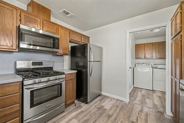 kitchen featuring a textured ceiling, stainless steel appliances, light hardwood / wood-style flooring, and washer and clothes dryer