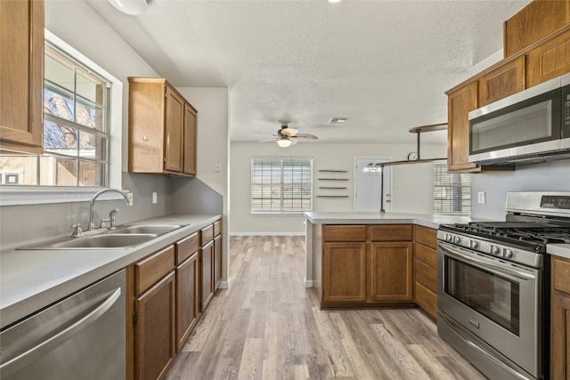 kitchen with sink, ceiling fan, light wood-type flooring, appliances with stainless steel finishes, and kitchen peninsula