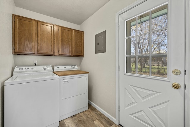 washroom featuring electric panel, washer and dryer, cabinets, and light wood-type flooring