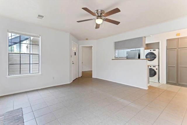 unfurnished living room featuring ceiling fan, light tile patterned floors, and stacked washer and clothes dryer