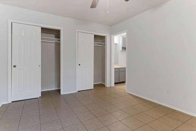 unfurnished bedroom with ceiling fan, light tile patterned floors, and multiple closets