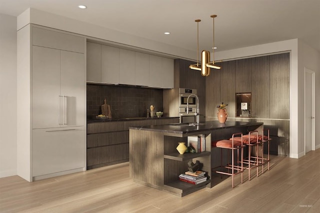 bar with dark brown cabinetry, hanging light fixtures, stainless steel double oven, and light wood-type flooring