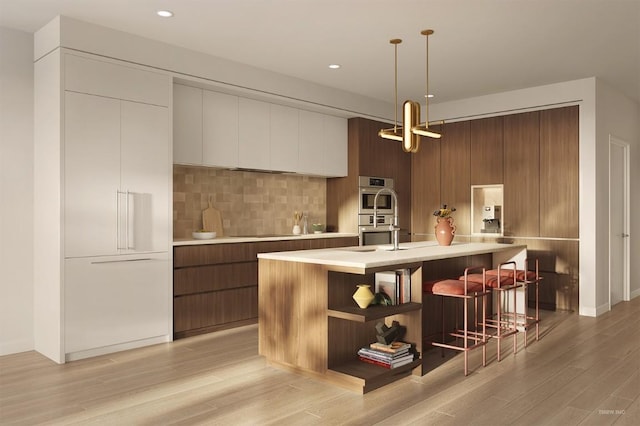 kitchen with double oven, pendant lighting, black electric cooktop, a center island with sink, and light wood-type flooring