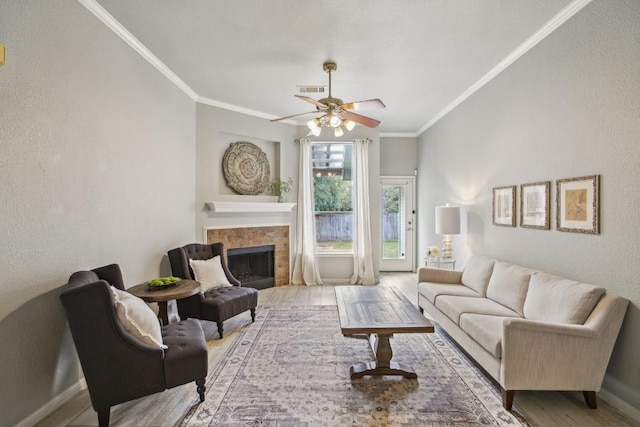 living room featuring ceiling fan, light wood-type flooring, ornamental molding, and a fireplace