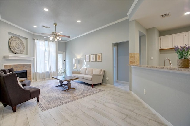 living room with a fireplace, sink, ceiling fan, light hardwood / wood-style floors, and crown molding