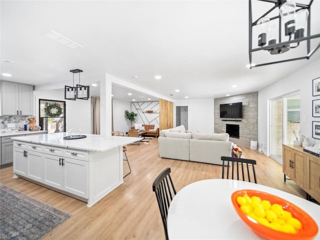 kitchen featuring white cabinets, a center island, decorative light fixtures, and a stone fireplace