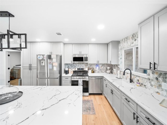 kitchen featuring appliances with stainless steel finishes, light stone counters, sink, light hardwood / wood-style floors, and hanging light fixtures