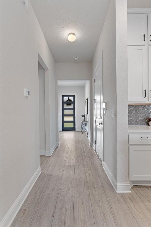 hallway with a textured ceiling and light hardwood / wood-style flooring