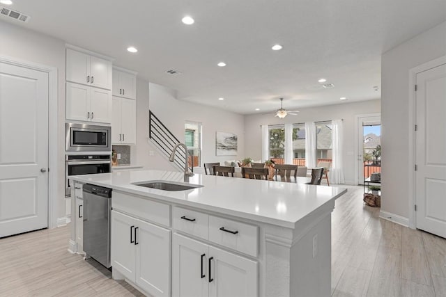 kitchen with sink, an island with sink, ceiling fan, stainless steel appliances, and white cabinets