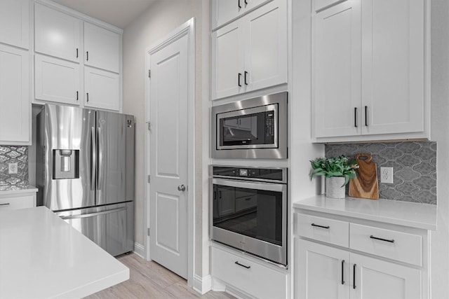 kitchen featuring decorative backsplash, light wood-type flooring, white cabinets, and appliances with stainless steel finishes