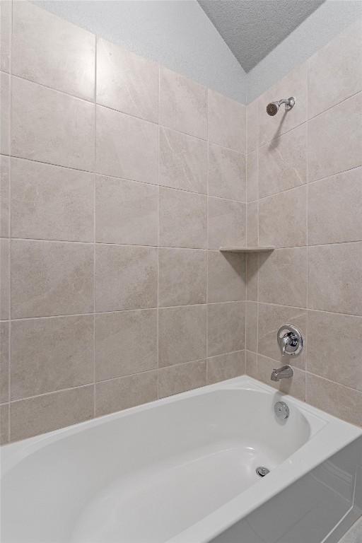 bathroom with lofted ceiling, tiled shower / bath combo, and a textured ceiling