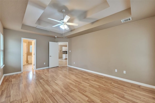 unfurnished bedroom featuring a tray ceiling, ceiling fan, light hardwood / wood-style floors, and ensuite bathroom