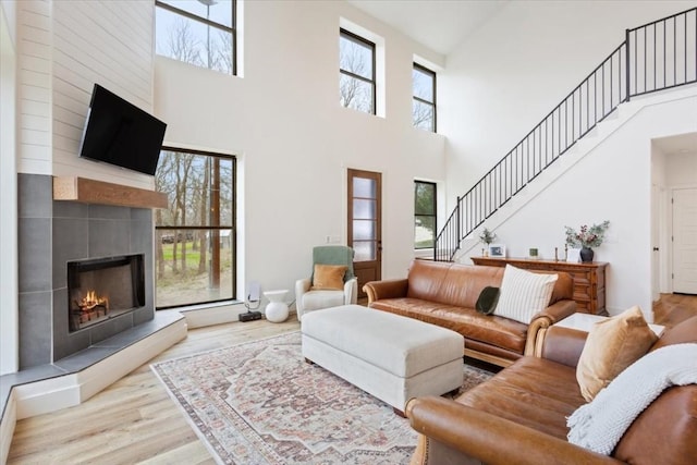 living room with a wealth of natural light, a fireplace, a towering ceiling, and light hardwood / wood-style flooring