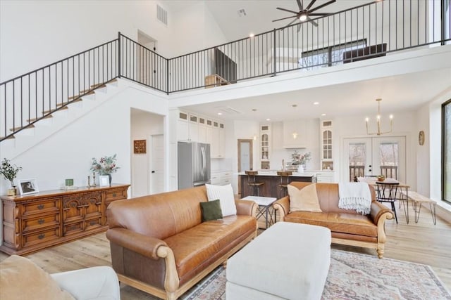 living room with a high ceiling, ceiling fan with notable chandelier, light hardwood / wood-style floors, and french doors