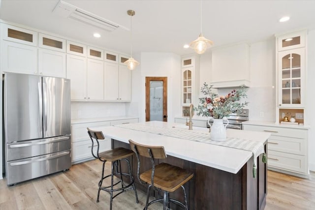 kitchen with premium range hood, white cabinets, hanging light fixtures, an island with sink, and appliances with stainless steel finishes