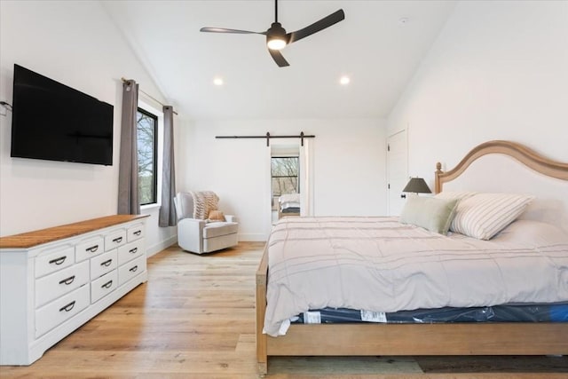 bedroom with a barn door, ceiling fan, lofted ceiling, and light wood-type flooring