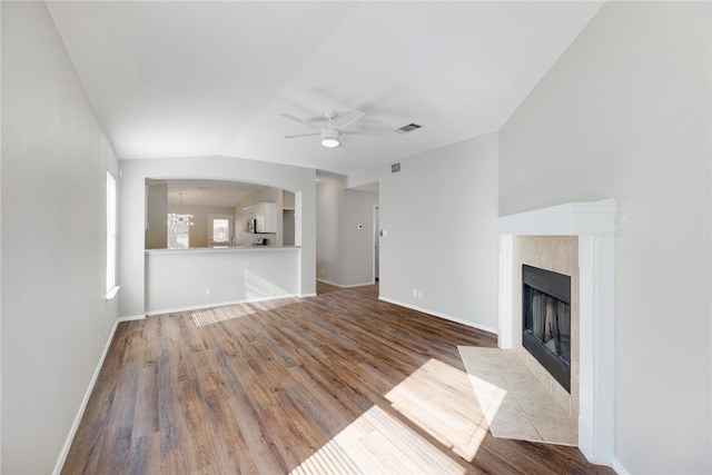 unfurnished living room featuring lofted ceiling, a fireplace, ceiling fan with notable chandelier, and light hardwood / wood-style flooring