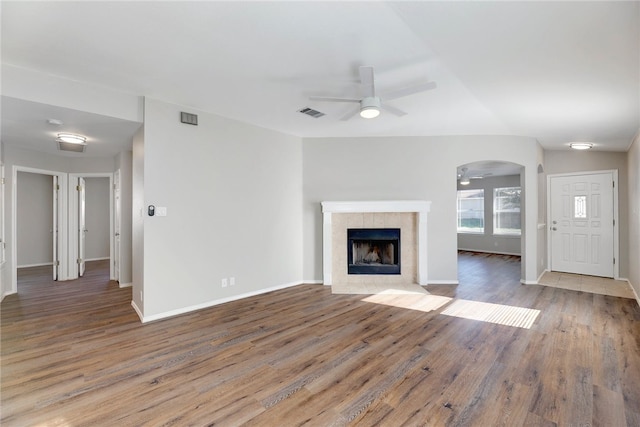 unfurnished living room with a tile fireplace, ceiling fan, and wood-type flooring