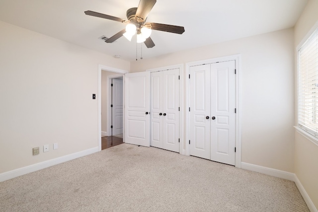 unfurnished bedroom with ceiling fan, multiple windows, light carpet, and two closets