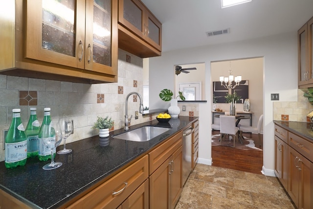 kitchen with dishwasher, sink, hanging light fixtures, dark stone countertops, and ceiling fan with notable chandelier