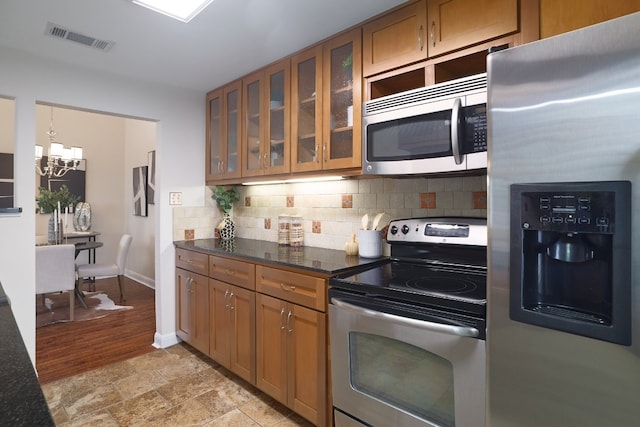 kitchen with decorative backsplash, stainless steel appliances, decorative light fixtures, an inviting chandelier, and dark stone countertops