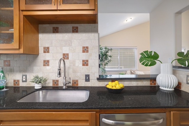 kitchen featuring dishwasher, dark stone counters, sink, vaulted ceiling, and tasteful backsplash