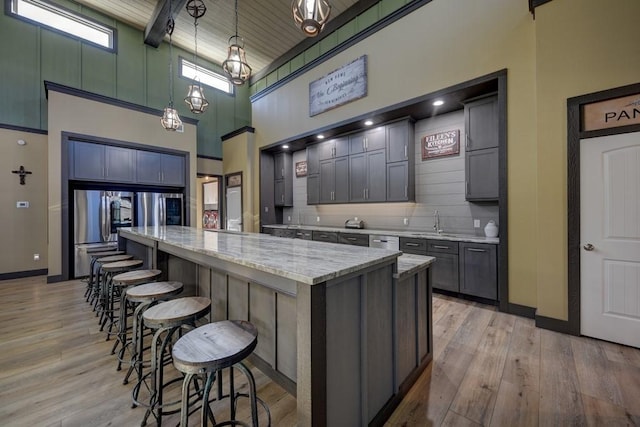 kitchen featuring hanging light fixtures, a high ceiling, stainless steel fridge, light hardwood / wood-style floors, and a kitchen island