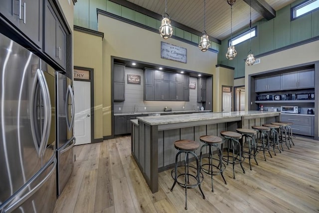 kitchen with stainless steel refrigerator, light stone countertops, a high ceiling, decorative light fixtures, and a kitchen island