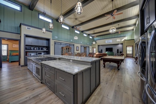 kitchen with appliances with stainless steel finishes, a high ceiling, a spacious island, and beam ceiling