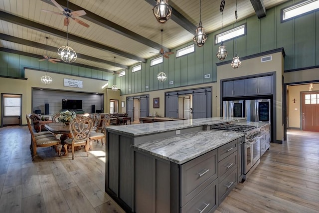 kitchen with appliances with stainless steel finishes, a spacious island, a barn door, high vaulted ceiling, and hanging light fixtures