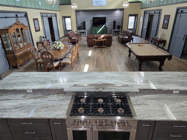 kitchen featuring light stone countertops, pool table, double oven range, hanging light fixtures, and hardwood / wood-style flooring