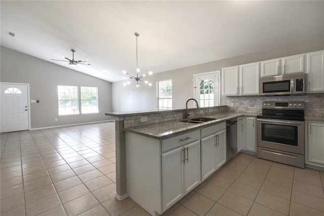 kitchen with sink, stainless steel appliances, kitchen peninsula, lofted ceiling, and light tile patterned floors