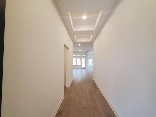 corridor with dark wood-style flooring, a raised ceiling, recessed lighting, and baseboards