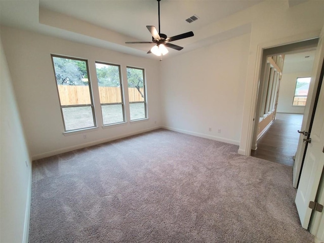 spare room featuring baseboards, visible vents, a raised ceiling, ceiling fan, and carpet floors