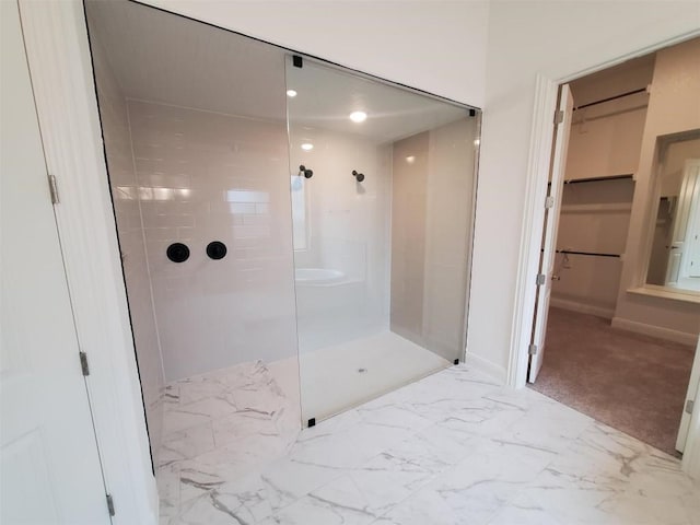 bathroom with marble finish floor, a spacious closet, walk in shower, and baseboards