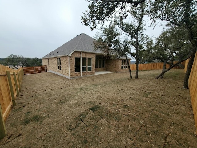 rear view of property featuring a patio area, a fenced backyard, a shingled roof, and brick siding