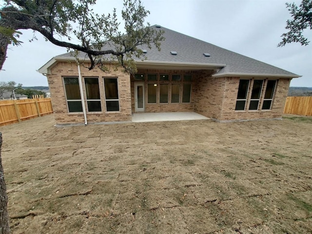 rear view of property with brick siding, roof with shingles, a fenced backyard, and a patio area