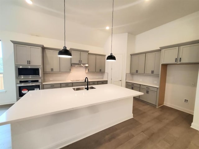 kitchen featuring an island with sink, decorative light fixtures, gray cabinets, stainless steel appliances, and light countertops