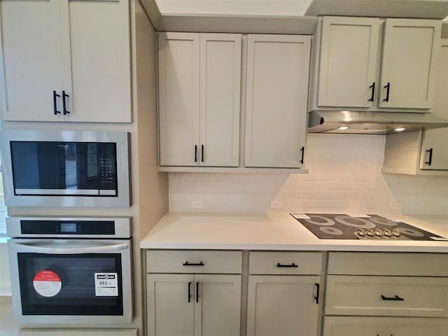 kitchen with light countertops, under cabinet range hood, stainless steel appliances, and decorative backsplash