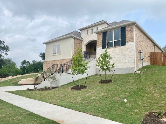 view of front of home featuring a front lawn, stone siding, stairway, and fence